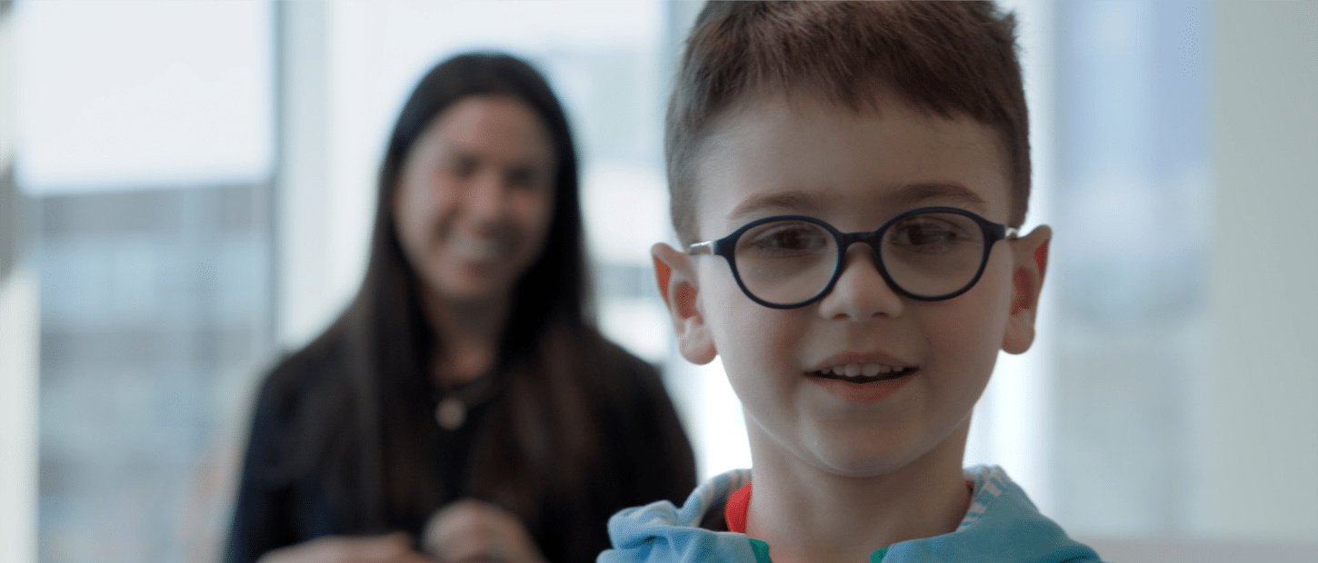 Boy wearing glasses with smiling woman in background